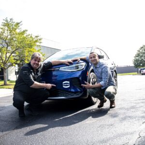 Zwei Männer hocken vor einem Auto: Rekord mit E-Auto
