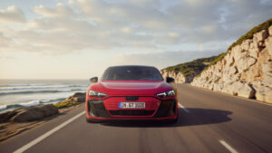 Roter Audi e-tron GT fährt an einer Küstenstraße entlang, Meer und Felsen im Hintergrund.