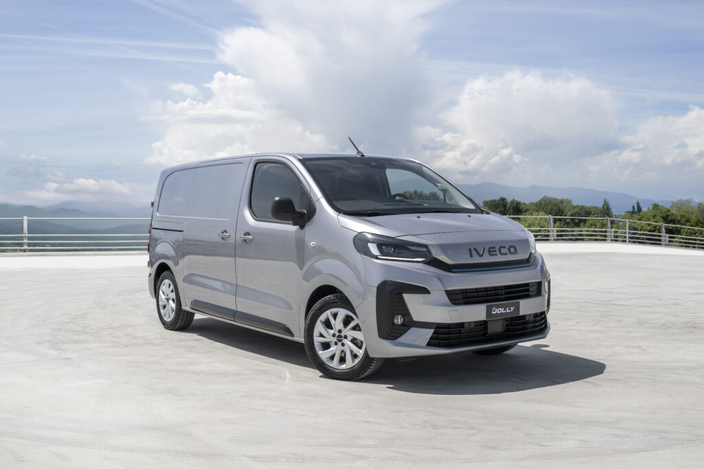 Der Iveco eJolly, ein kompakter Elektrotransporter, steht auf einem offenen Platz mit Bergen im Hintergrund.