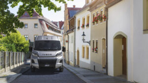Ein Iveco eSuperJolly fährt durch eine enge Gasse in einer historischen Altstadt mit blumengeschmückten Häusern.