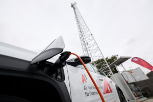 Nahaufnahme eines Renault E-Autos mit eingestecktem Ladekabel, im Hintergrund ein Mobilfunkmast.