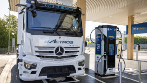 Ein weißer Elektro-Lkw Mercedes-Benz eActros lädt an einer modernen Schnellladestation von Siemens bei einer OMV-Tankstelle.