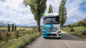 Ein Mercedes-Benz eActros 400 fährt auf einer Landstraße durch eine grüne Landschaft. Auf der Fahrzeugfront steht der Schriftzug „Charged to Change“.