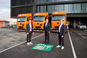 Drei orange eActros 600 vor Logistikzentrum mit Personen